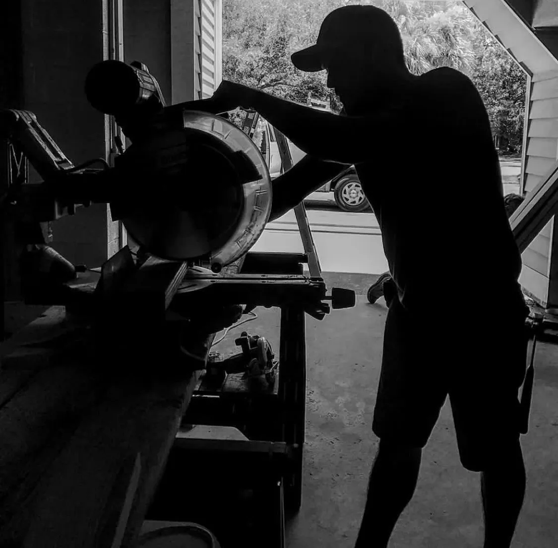 Adam Seigler cutting a board at his miter saw, silhouetted in the open shop door